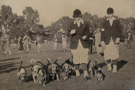 Black and white photo of two people walking with hounds
