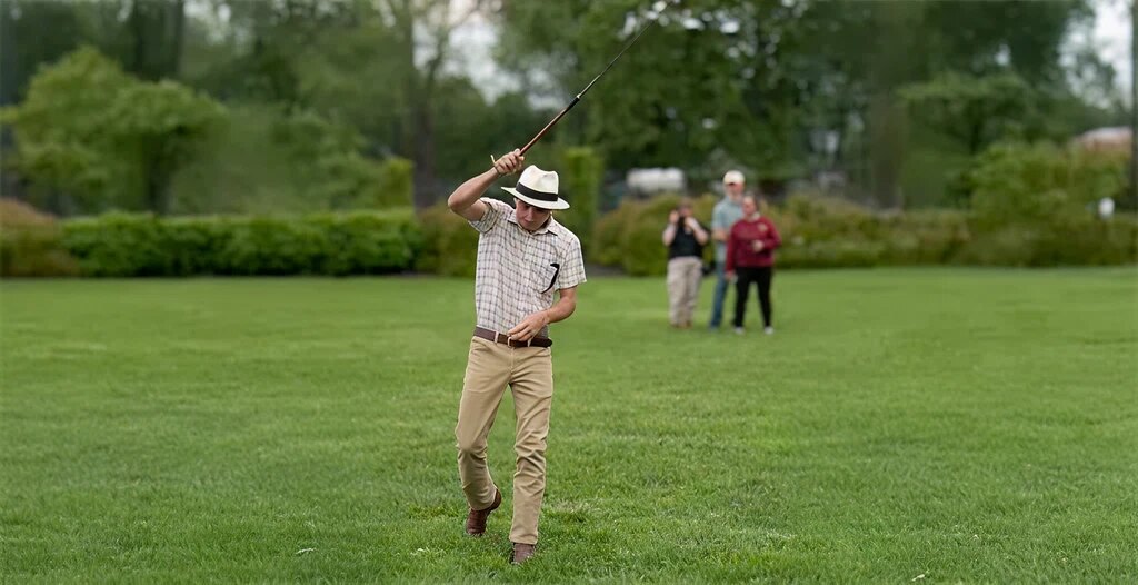 Person with hat swinging stick